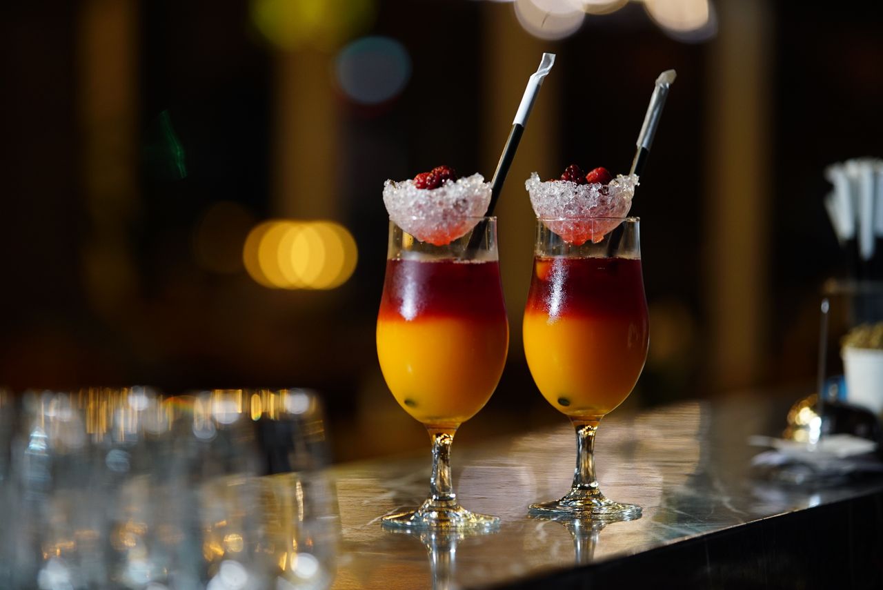 about-us Two vibrant cocktails with berries and ice, set in a stylish bar setting.
