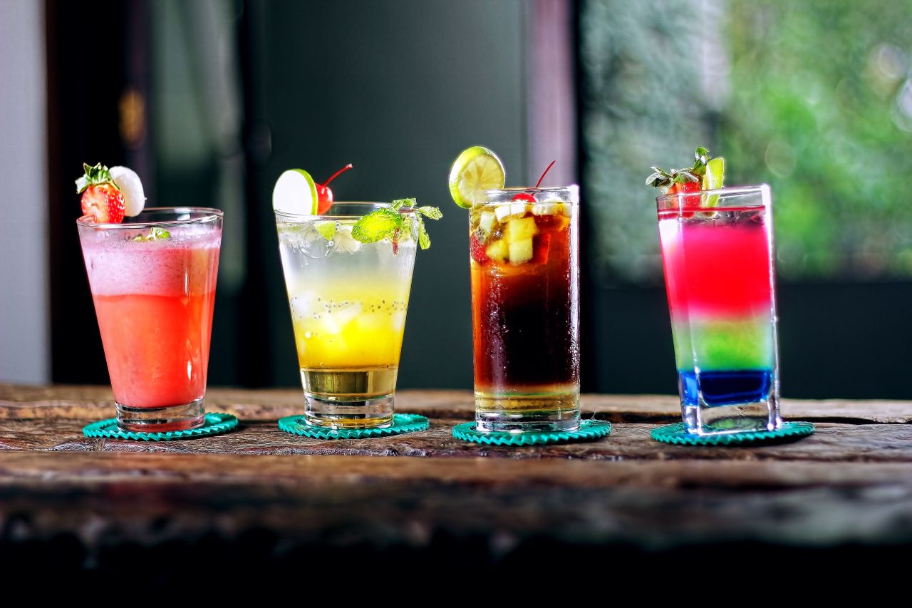 heros-img Colorful assortment of cocktails on a rustic wooden table, perfect for a refreshing summer evening.